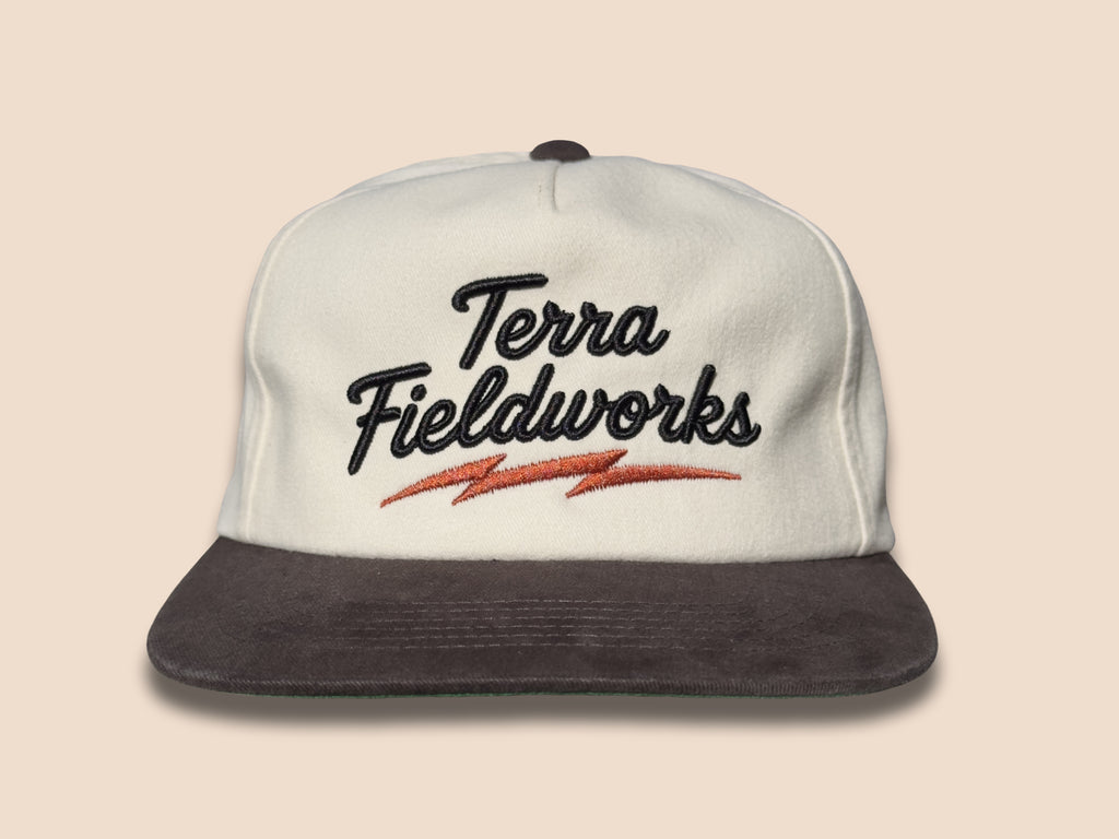 Lightning Bolt Snapback Hat in cream/black with black puff embroidered Terra Fieldworks script and orange lightning bolt
