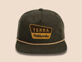 A moss green nylon and cotton hybrid cap with a flat brim, featuring a yellow and brown embroidered patch on the front in the style of the National Forest sign that reads 'TERRA Fieldworks', set against a solid beige background.

"National Forest" rope hate in moss green/cream with Terra Fieldworks patch embroidery styled after the "National Forest" signage. 